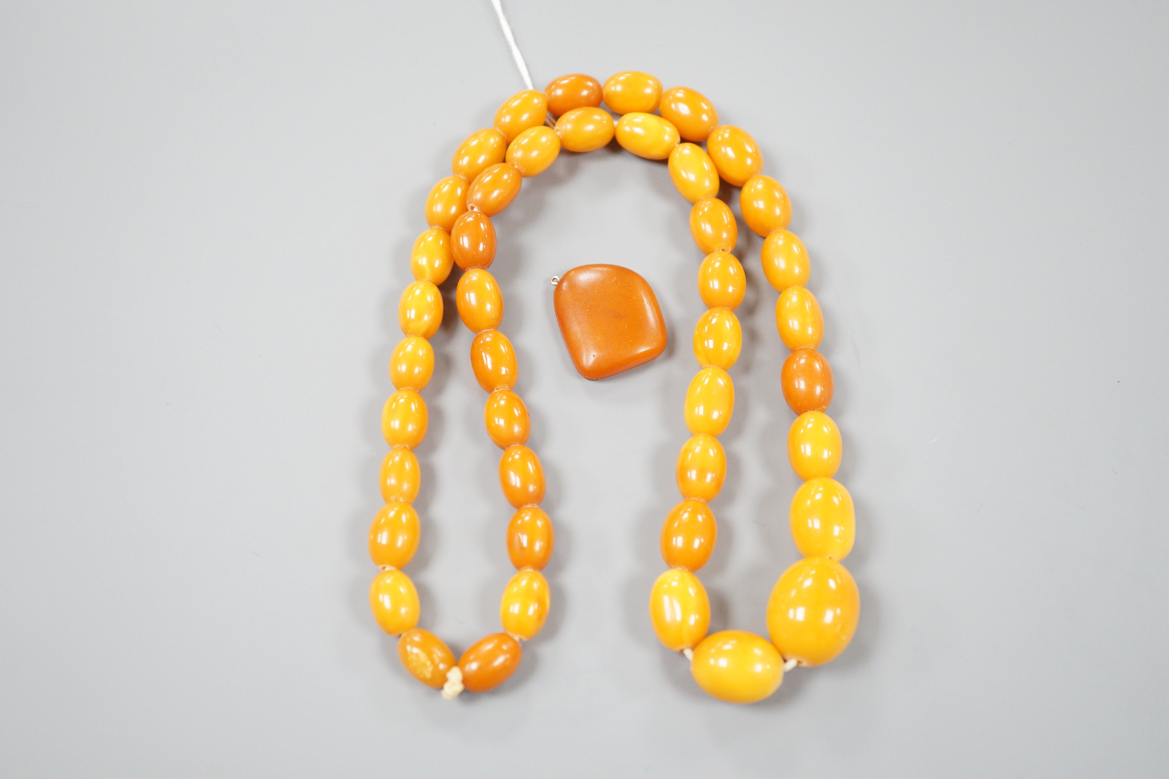 A single strand graduated oval amber bead necklace, 70cm, gross weight 64 grams, together with an amber pebble pendant, gross 5 grams.
